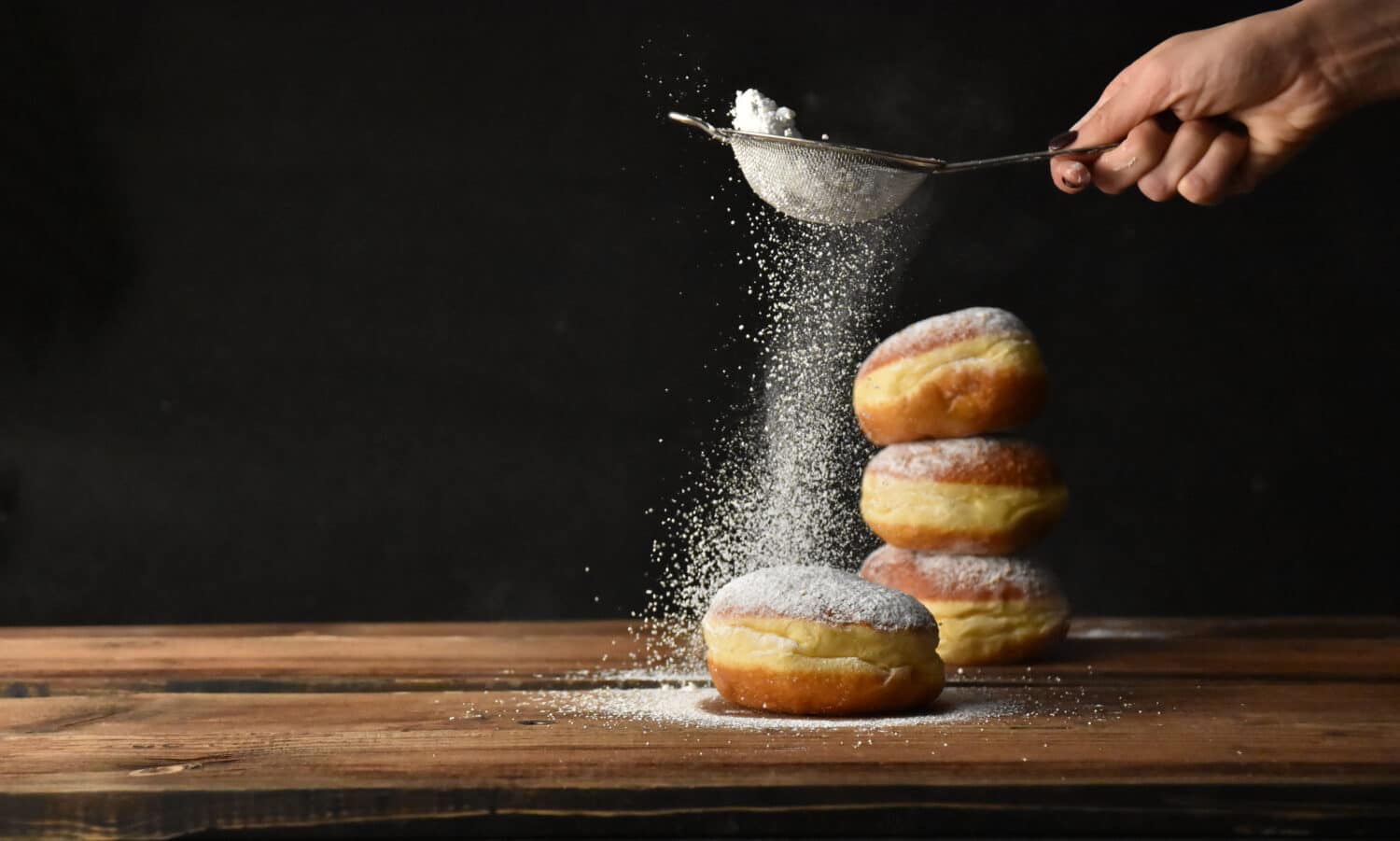 European donut sprinkled with powdered sugar on black background
