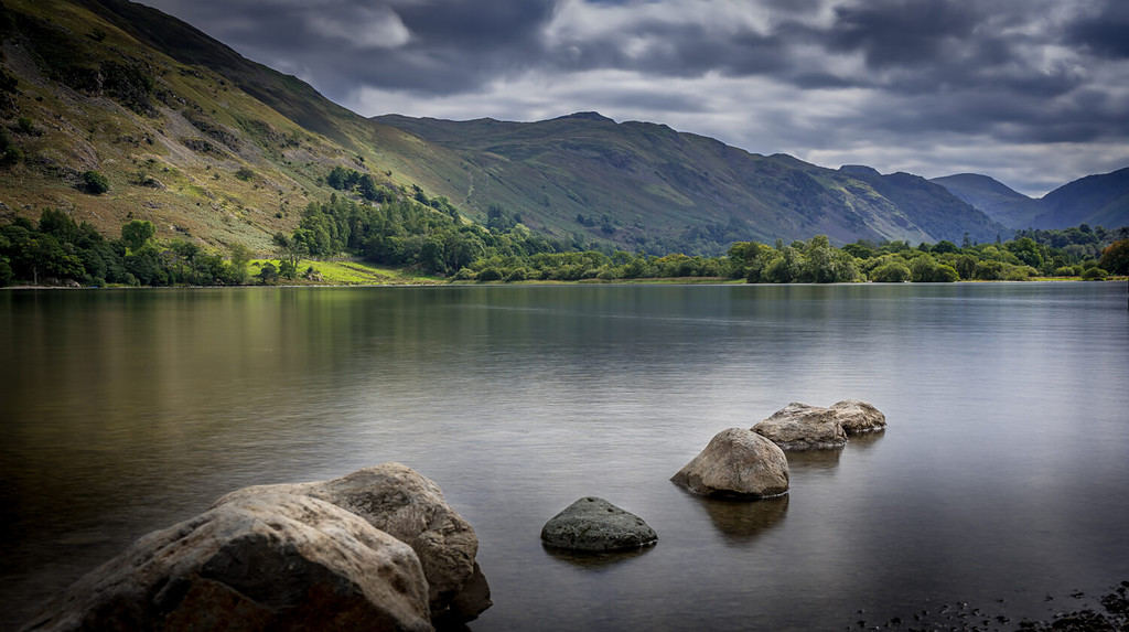 Moody view looking out across a calm waters at Ullswater Lake with mountains in the distance in The Lake District, Cumbria, UK