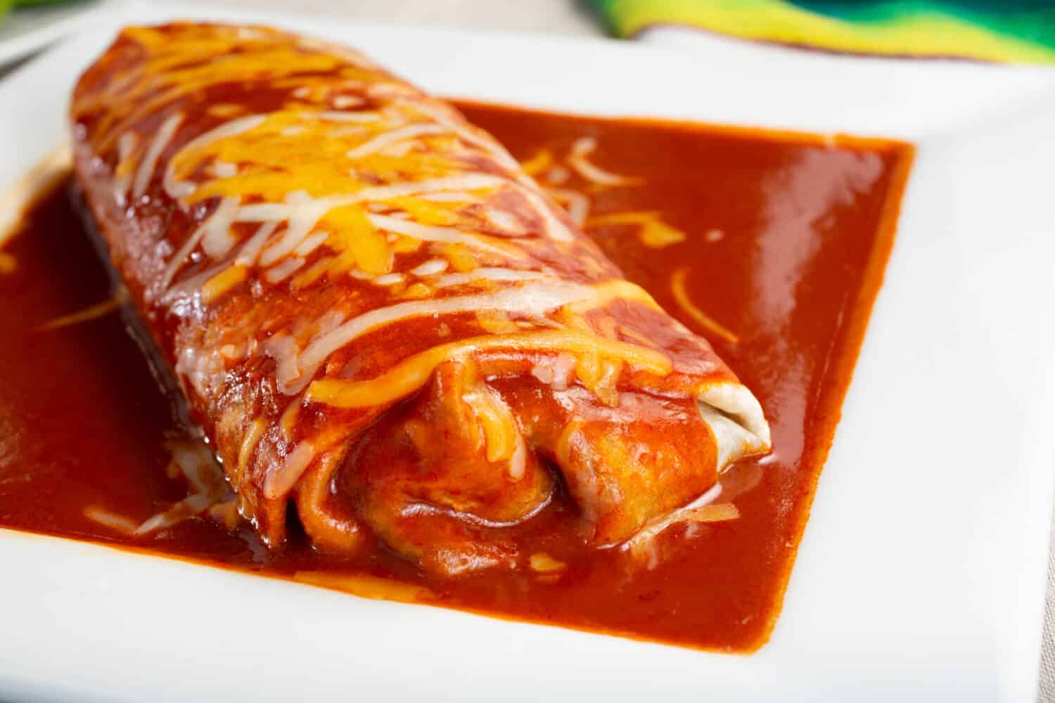 A closeup view of a wet burrito on a plate.