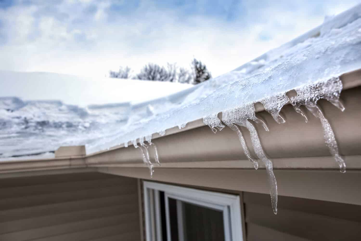 Ice dam in gutter and ice frozen on roof in winter, shallow focus on icicles in foreground 