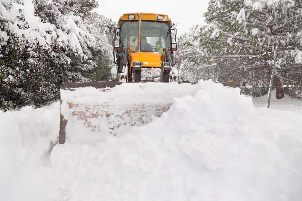 Yellow tractor removes a pile of snow from a road in El Berrueco, Madrid.