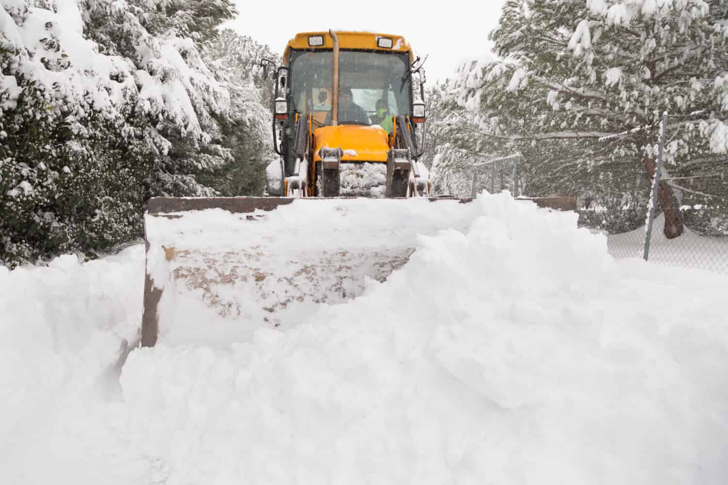 Yellow tractor removes a pile of snow from a road in El Berrueco, Madrid.