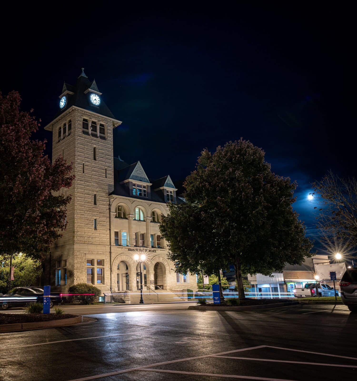 Richmond, Kentucky's Madison County courthouse at night with a full moon behind it and evening traffic crossing in front of the building