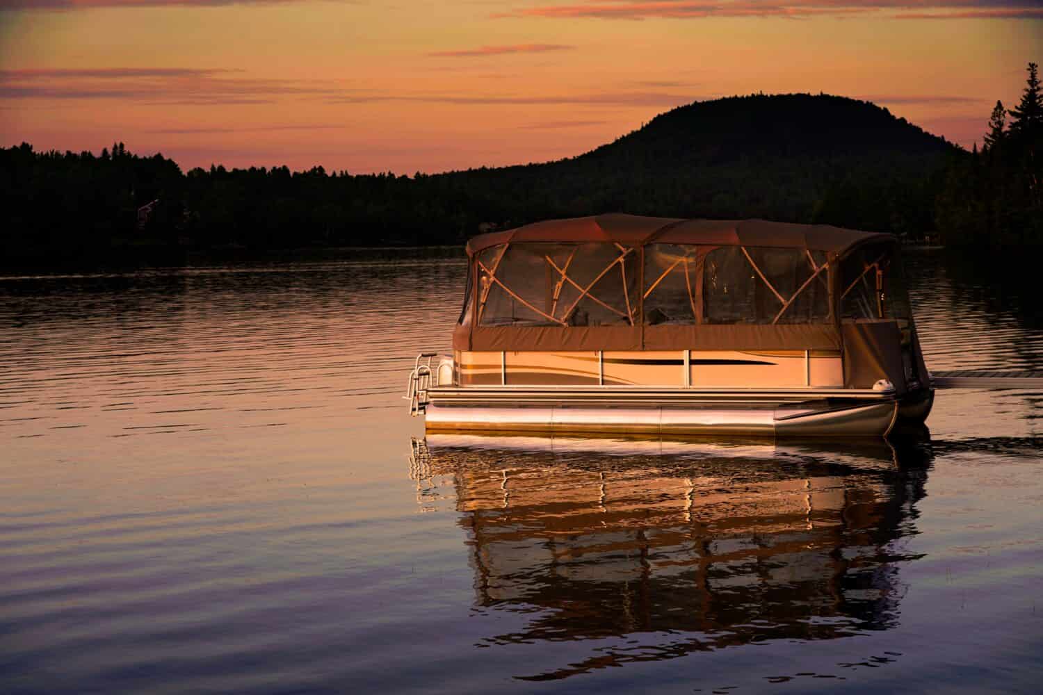 A picture of a pontoon boat on lake with a evening sunset