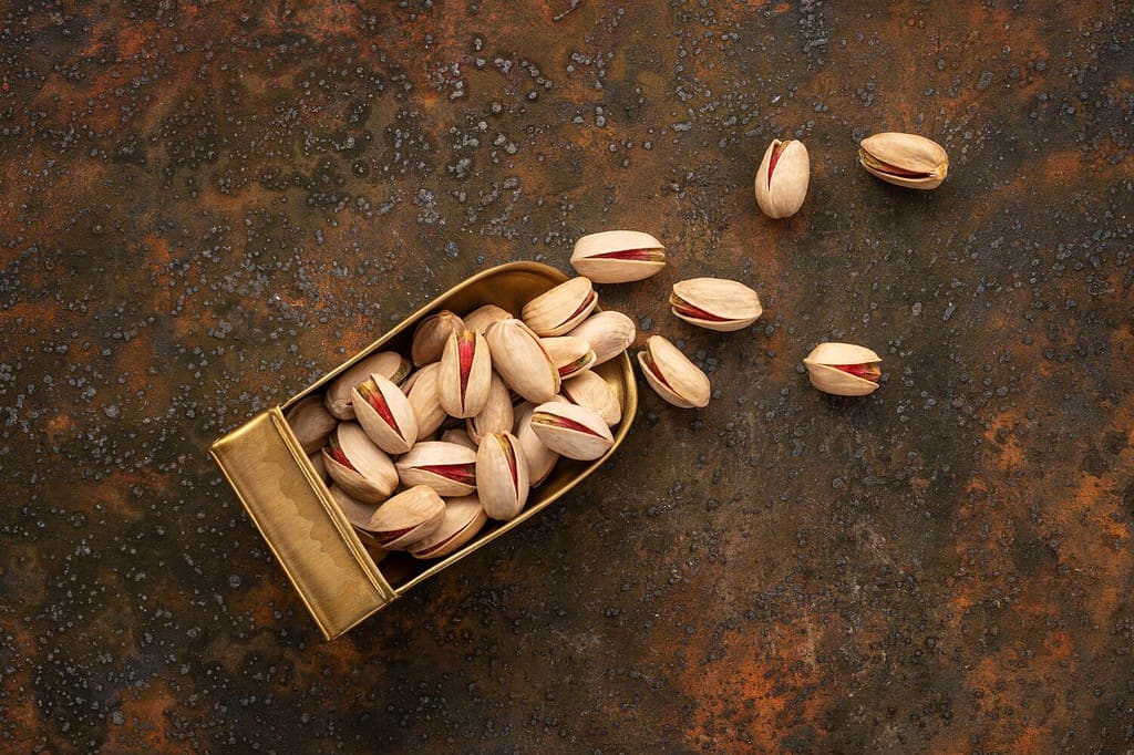 Top View of Whole Pistachios in A Brass Scoop on A Rustic Background