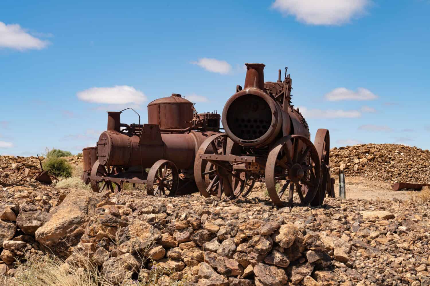 Two old mining steam engines in the desert at Silverton, New South Wales, Australia. Fluffy white clouds in blue sky.