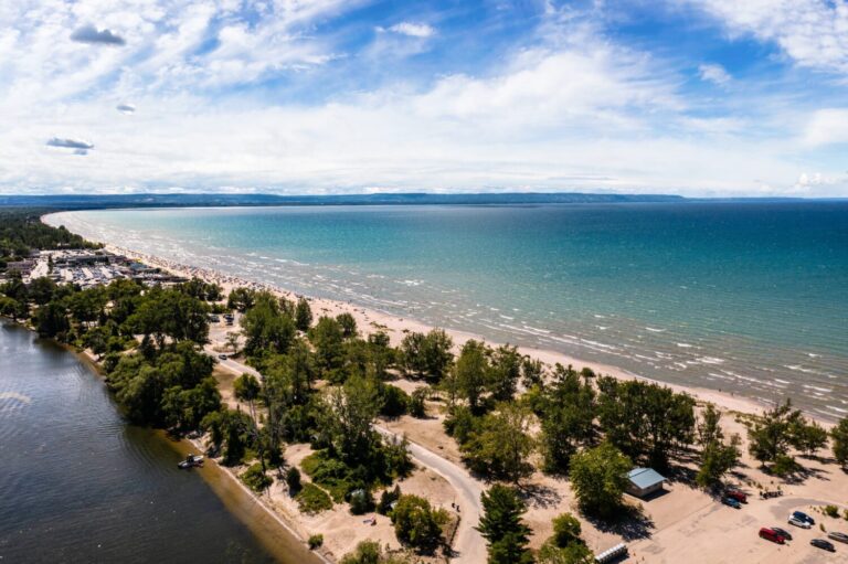 "Soar above Wasaga Beach with this mesmerizing drone photo. The image captures the beach under a beautiful blue sky dotted with fluffy clouds, exuding an air of tranquility and freedom."