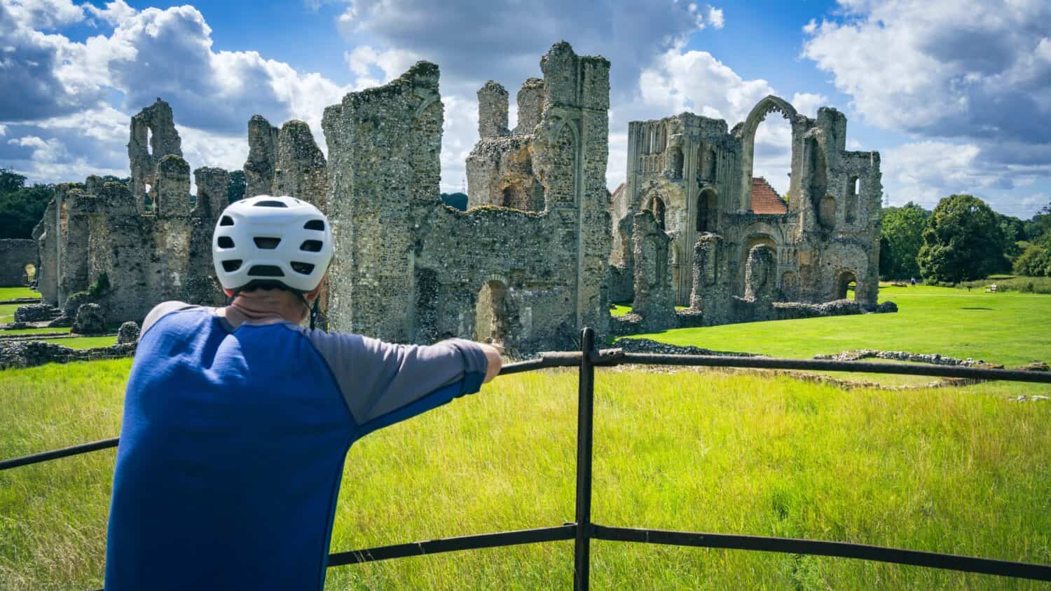 A man wearing a cycle helmet looks at the ruins of Castl Acre Priory in Kings Lynn Norfolk England UK