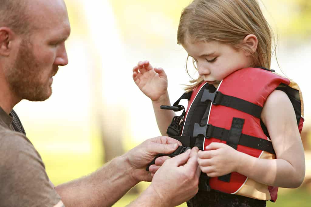 A father helping his daughter with her life jacket