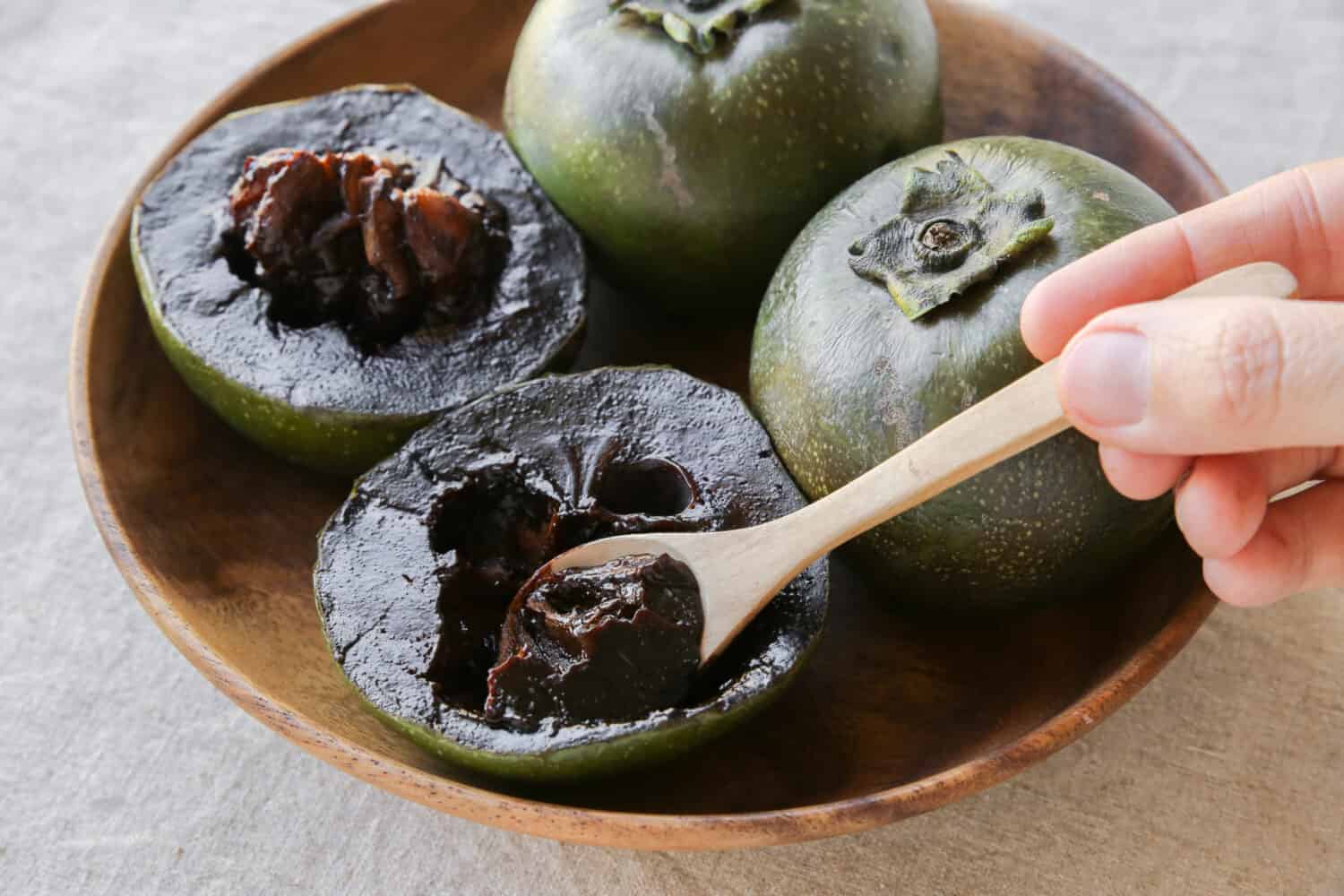 Black sapote chocolate pudding fruit in wooden plate, plant based vegan food