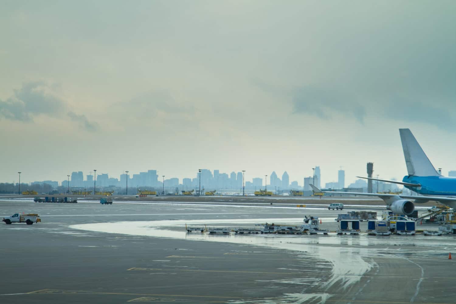 The tarmac at an airport, showing the rear of a passenger plane and service vehicles surrounding it, with a skyline of a city behind.  Pearson International airport, Toronto, Ontario.