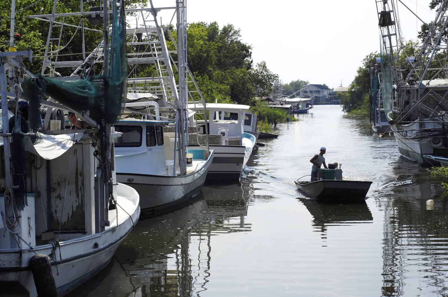 A lone fisherman poles a flatboat along a canal in Lafitte, Louisiana, lined with shrimp boats.