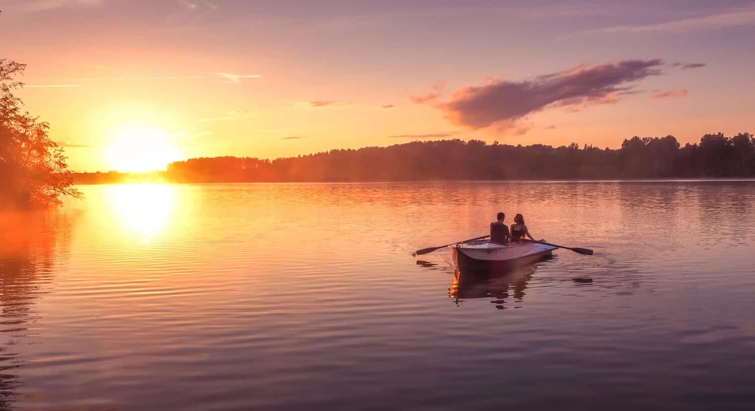 A beautiful golden sunset on the river. Lovers ride in a boat on a lake during a beautiful sunset. Happy couple woman and man together relaxing on the water. The beautiful nature around. 
