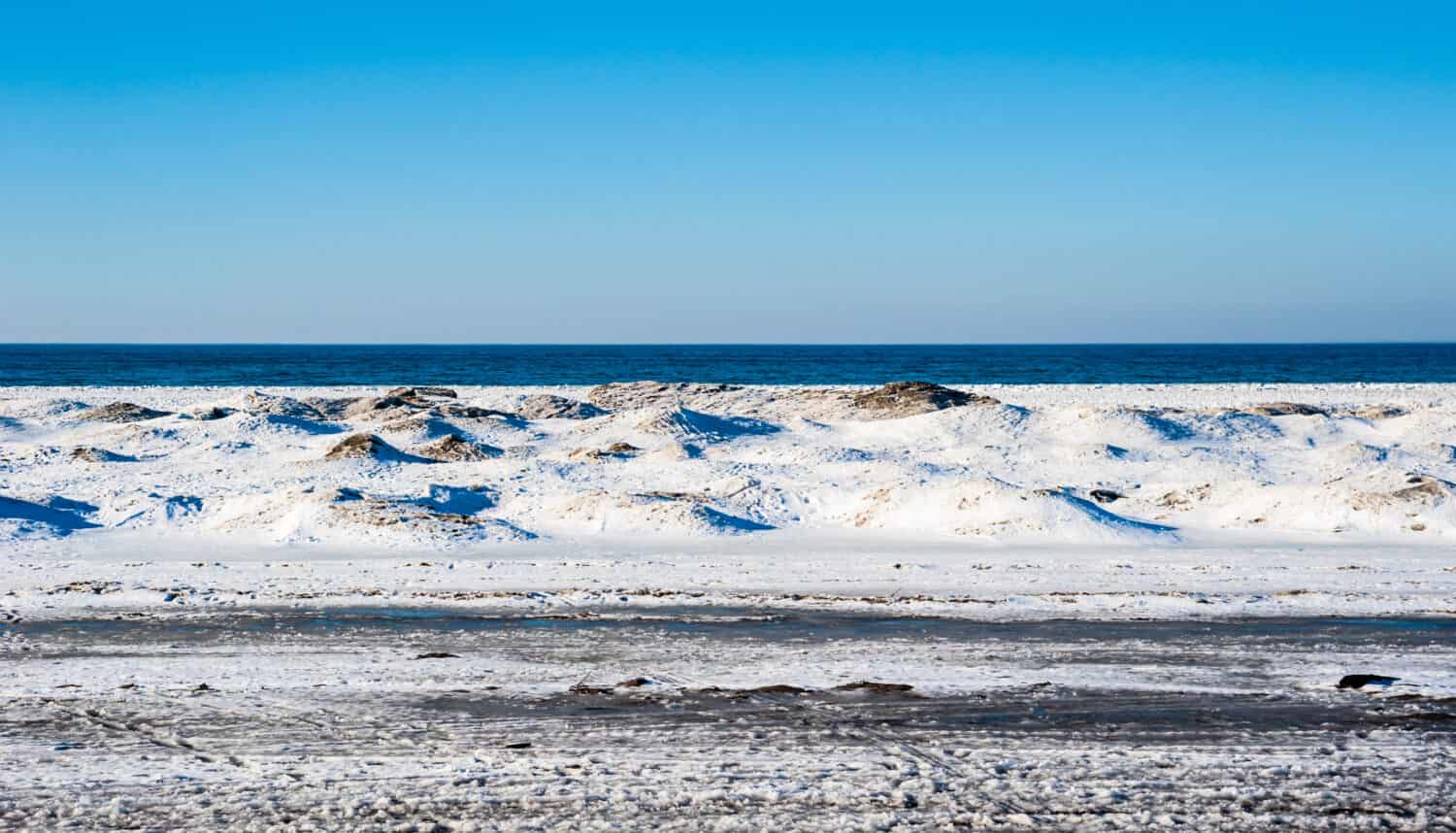 Frozen ice and sand dunes on beach in winter by empty lake horizon under clear blue sky, near Georgian Bay, Ontario, Canada.
