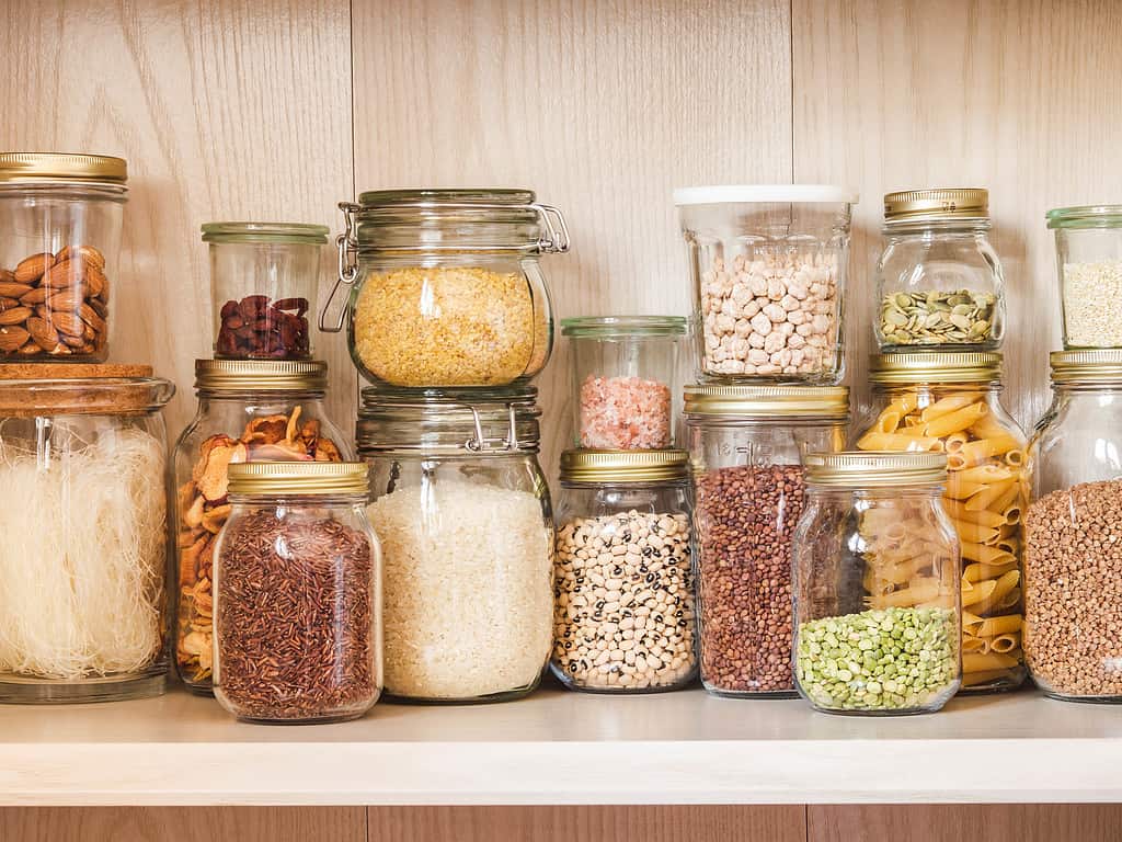Shelf in the kitchen with various cereals and seeds - peas split, sunflower and pumpkin seeds, beans, rice, pasta, oatmeal, couscous, lentils, bulgur in glass jars