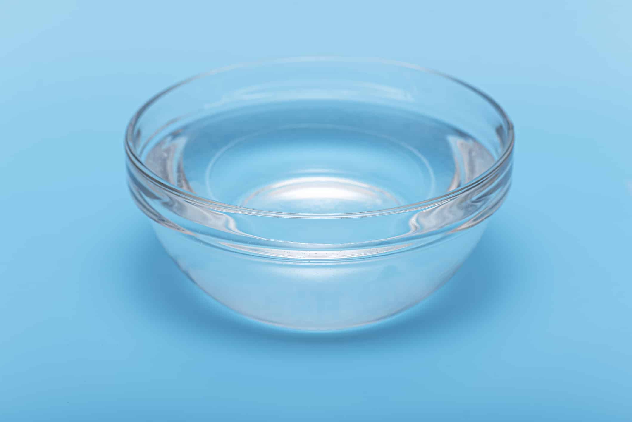 Pure, clear drink water in glass bowl or plate on blue background