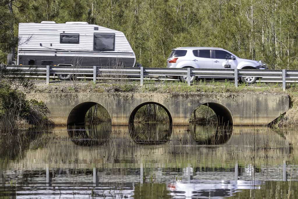 Car and caravan driving across culverts under a road, Durras Lake, NSW, October 2021