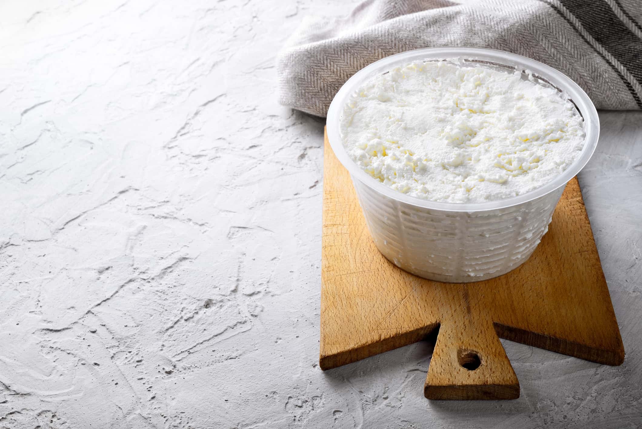 Ricotta cheese and wooden cutting board on white plaster background. Space for text.