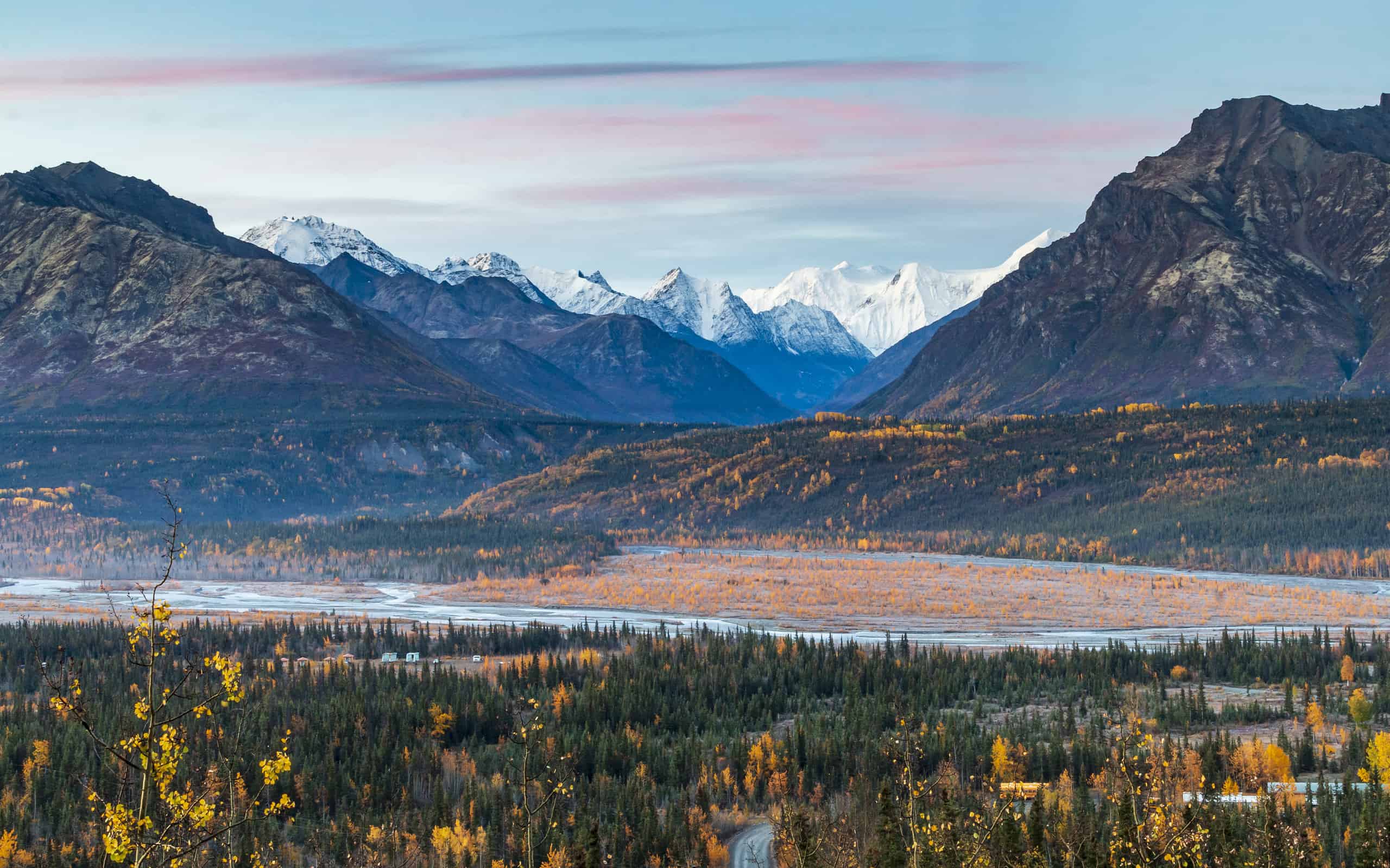 dramatic landscape of golden yellow autumn foliage of aspen and birch trees and snowcapped mountains of the Chugach mountain range in Alaska.