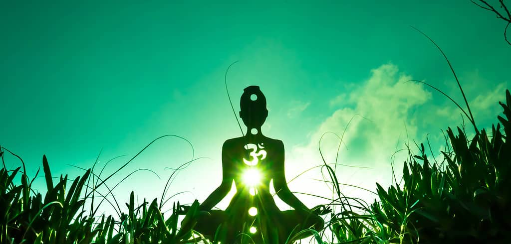 Green shining through silhouette in meditative pose.