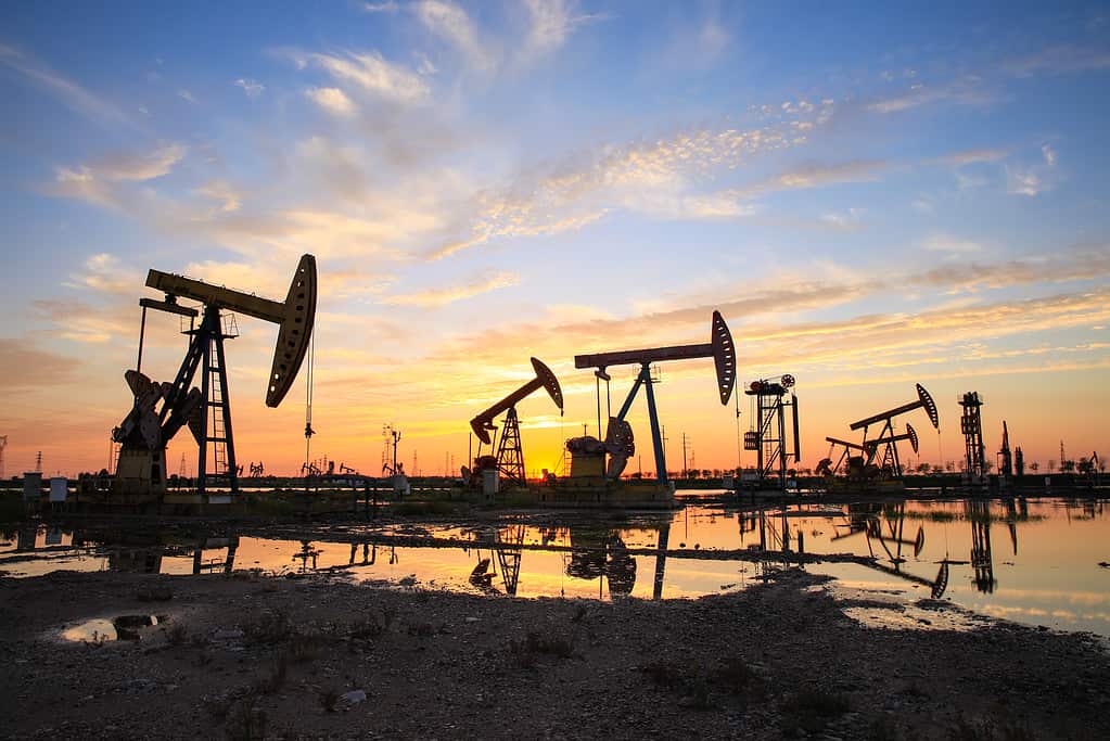 Oil field site, in the evening, oil pumps are running, The oil pump and the beautiful sunset reflected in the water