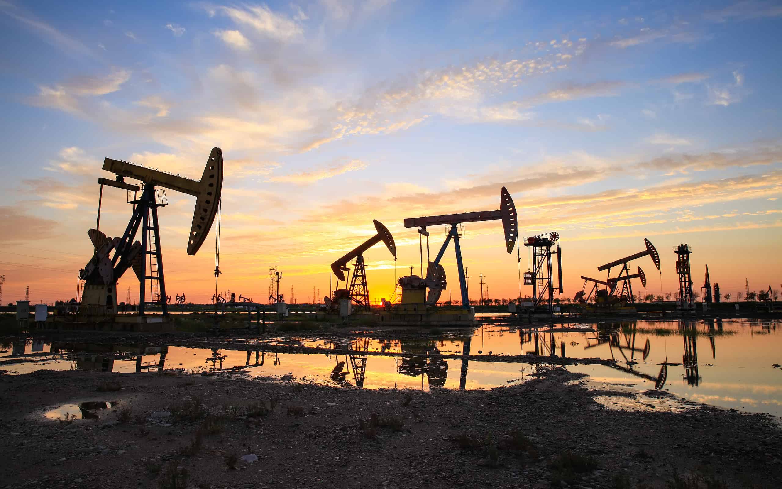 Oil field site, in the evening, oil pumps are running, The oil pump and the beautiful sunset reflected in the water
