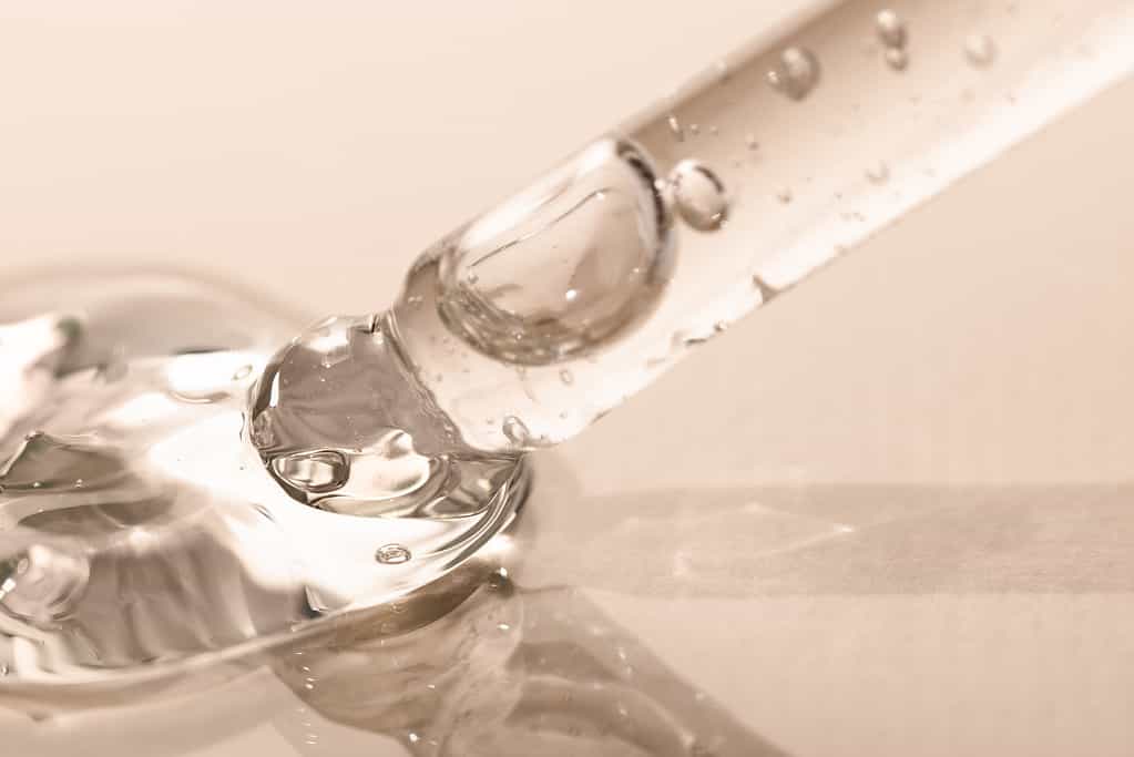 Liquid transparent cosmetic drop with bubbles and a pipette on a light background, macro. Tool for beauty procedures for body care.