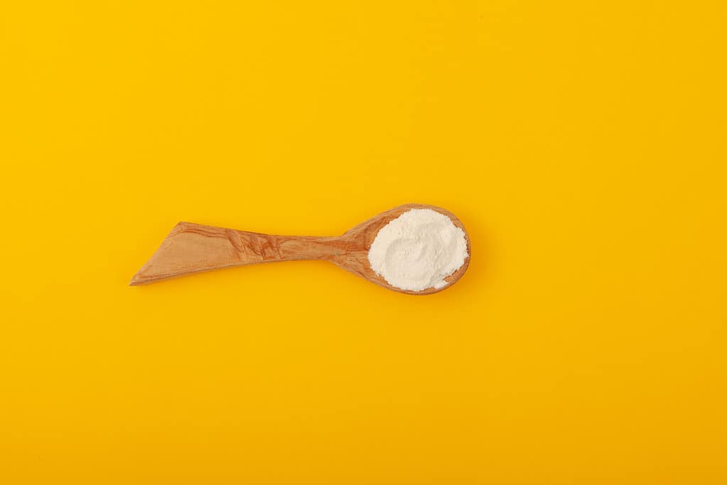 Xanthan Gum Powder in wooden spoon on yellow background, top view. Food additive E415. Suspending & Granulating agent, Texture improver. Gluten free products