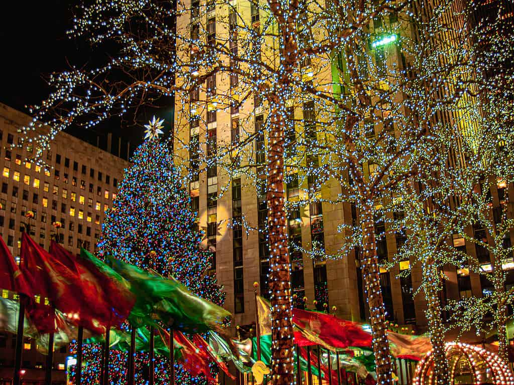 Holiday flags and the Christmas tree on a windy night in Rockefeller Center, New York City.