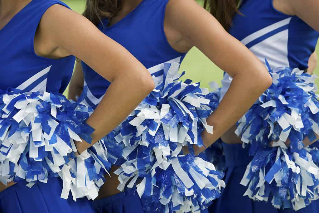 Three cheerleaders in blue and white uniform and pom-poms