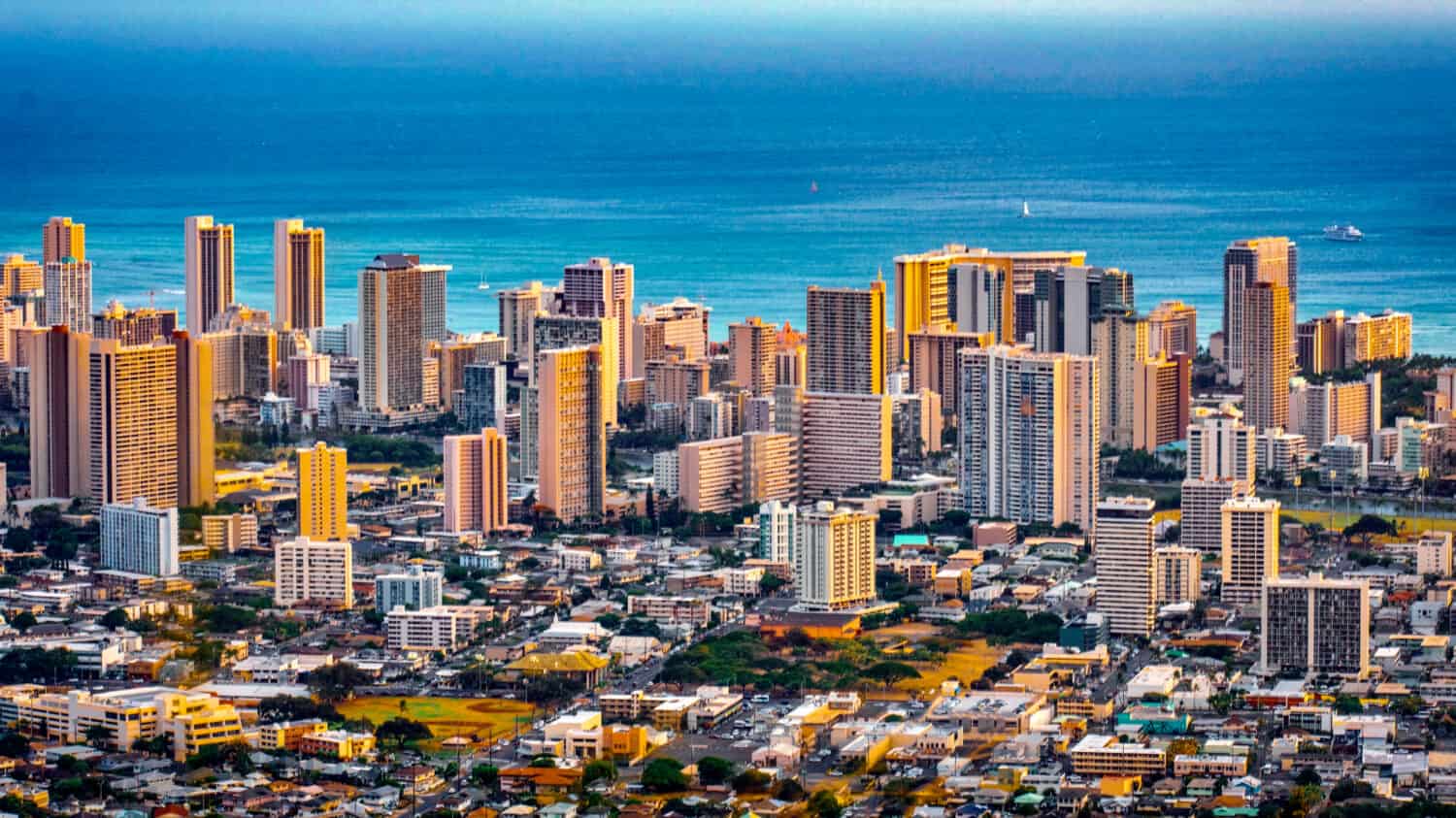 Cityscape of Honolulu city and  Waikiki beach with blue ocean and light reflection from sunset sky to buildings from Ualaka’a lookout on Tantalus mountain  in Honolulu, Oahu, Hawaii USA