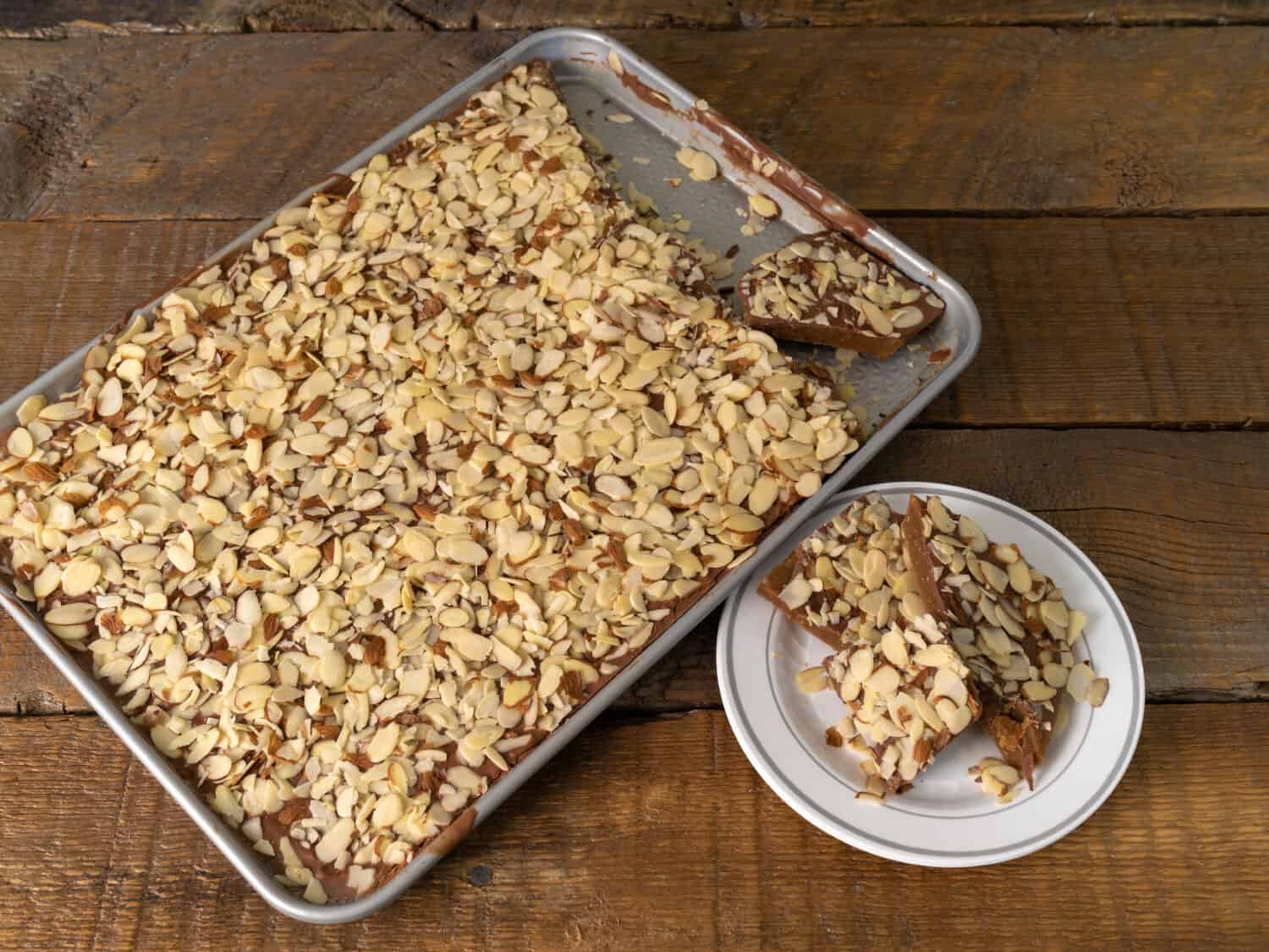 Homemade Almond Roca candy in a pan and a plate on a wood background. 