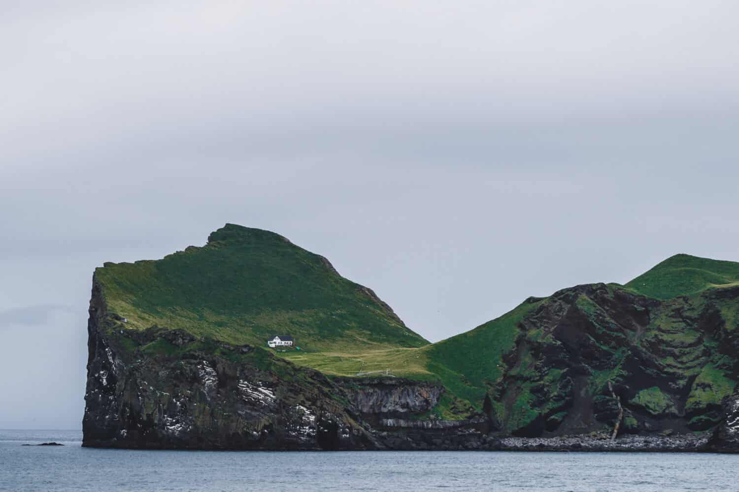 Lonely house on Ellidaey island in Vestmannaeyjar archipelago, Iceland. Rocky and green island. Nordic landscape.