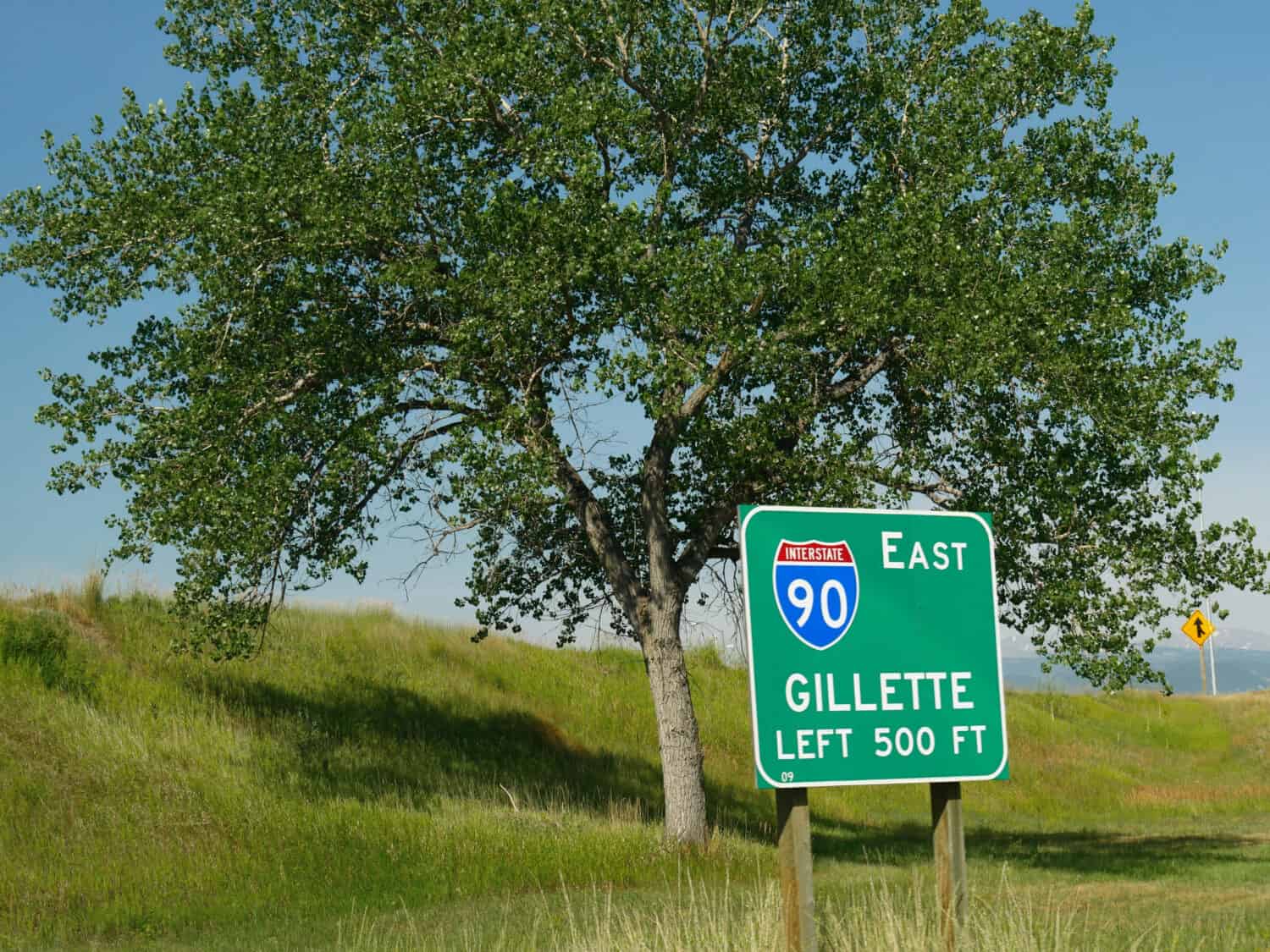 Roadside sign by a tree at Interstate 90 with distance to Gillette, Wyoming.