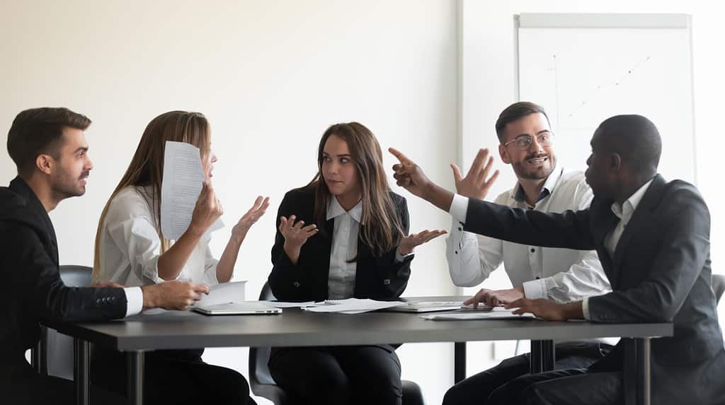 Mad frustrated multiethnic employees sit at office meeting dispute quarrel have stressful job situation, angry diverse colleagues debate fight over paperwork financial statistics, work stress concept
