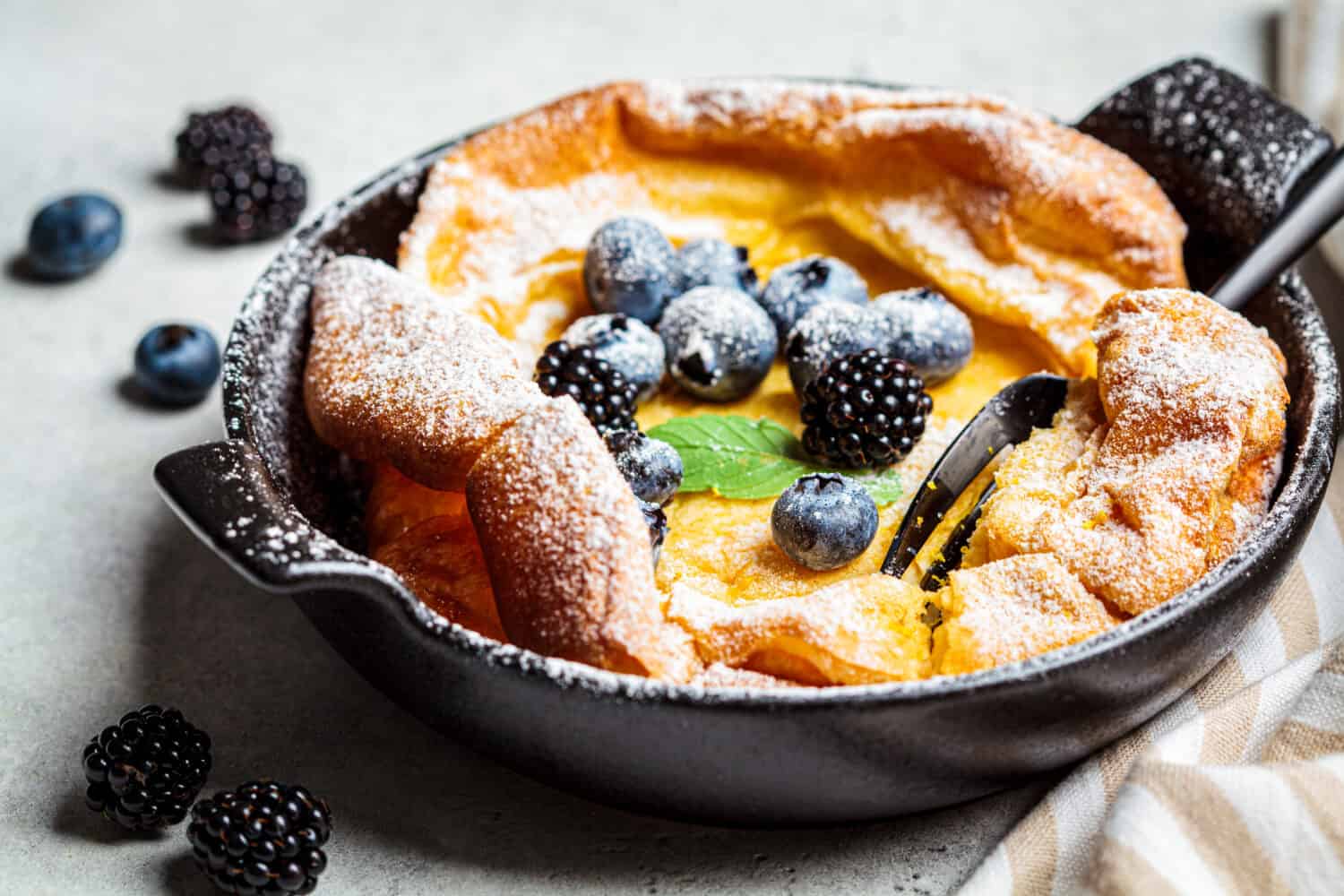Dutch baby pancake with berries and icing sugar in a pan.