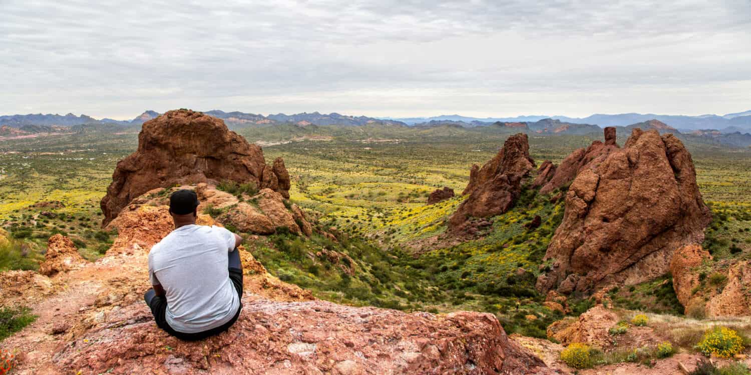African American man contemplating the view from The Flatiron in the Superstition Mountains from Treasure Loop Trail. Black hiker in the Arizona desert panoramic. Moutain peak hiking banner. 