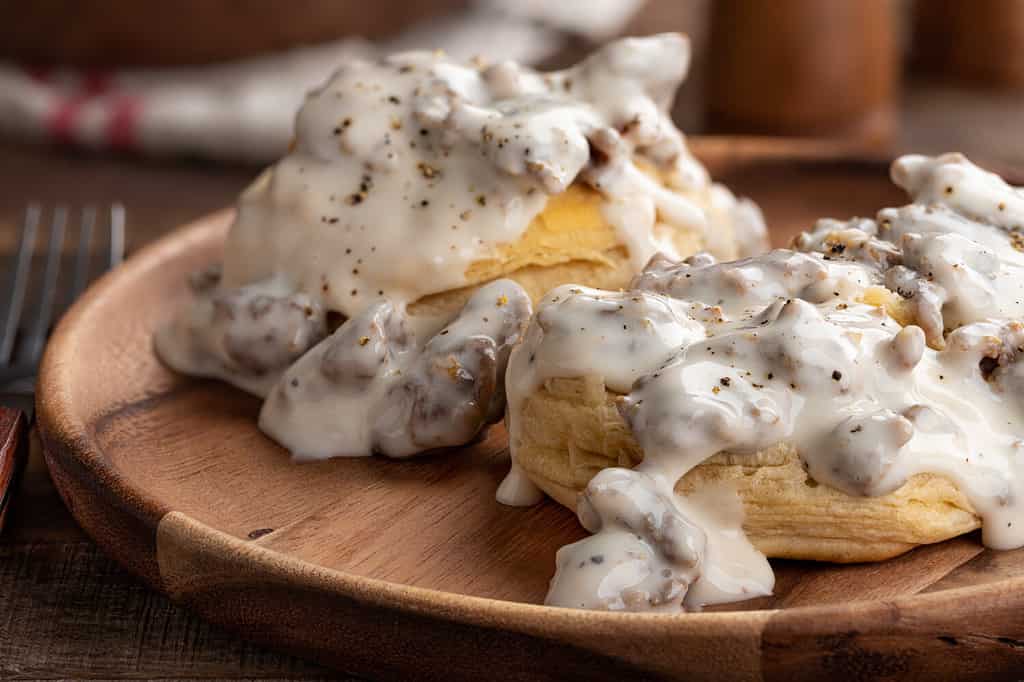 Closeup of biscuits and creamy sausage gravy on a wooden plate