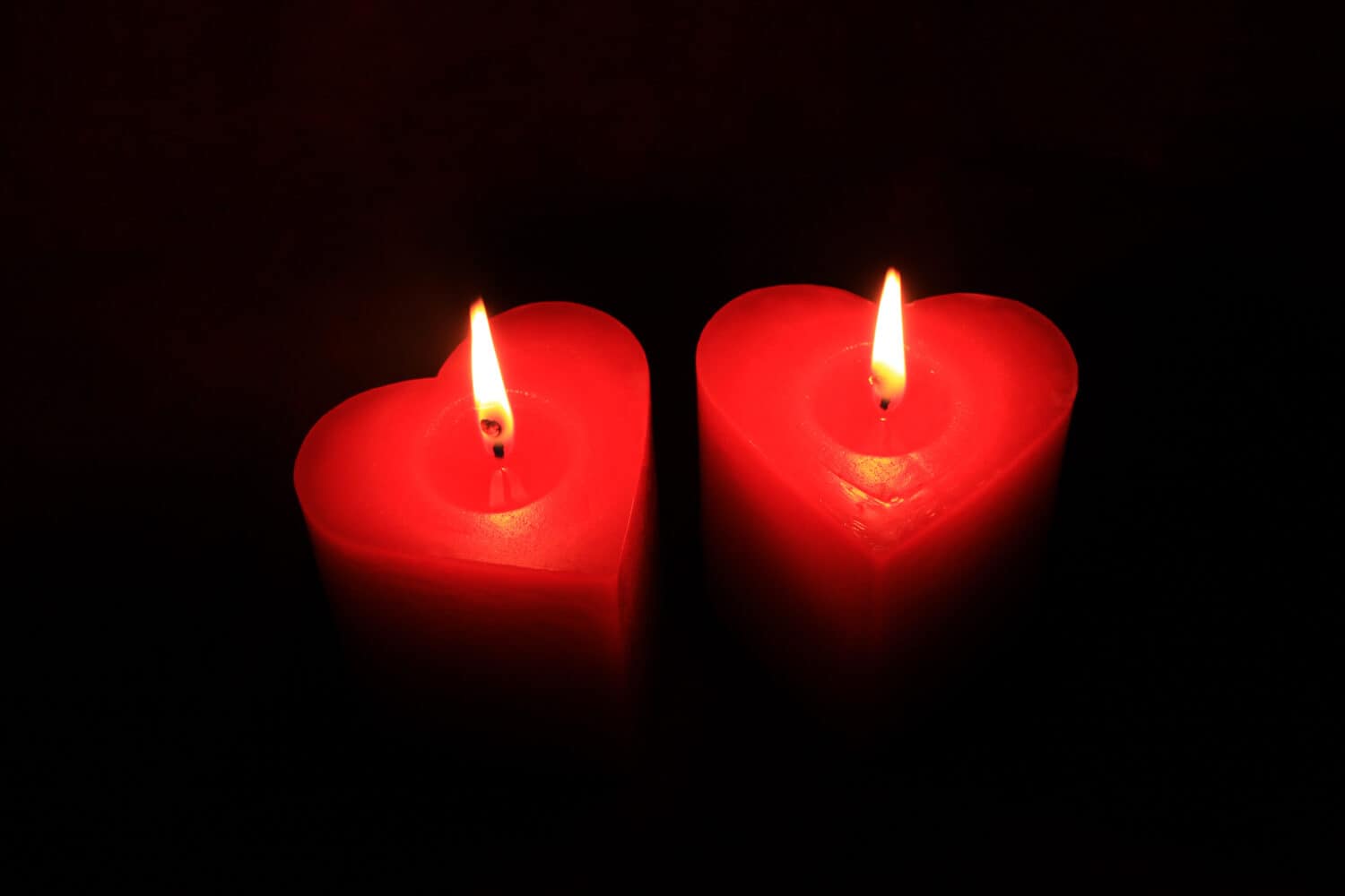 Two flames burning in dark . Two heart shaped red candles on black background