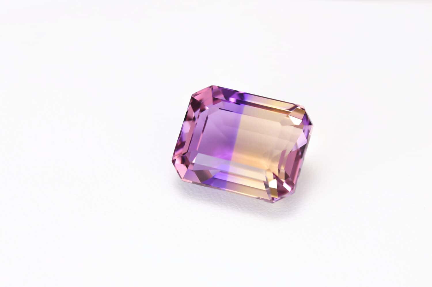Loose natural bicolor: purple and yellow, Bolivian ametrine emerald cut faceted gemstone on white leather textured background