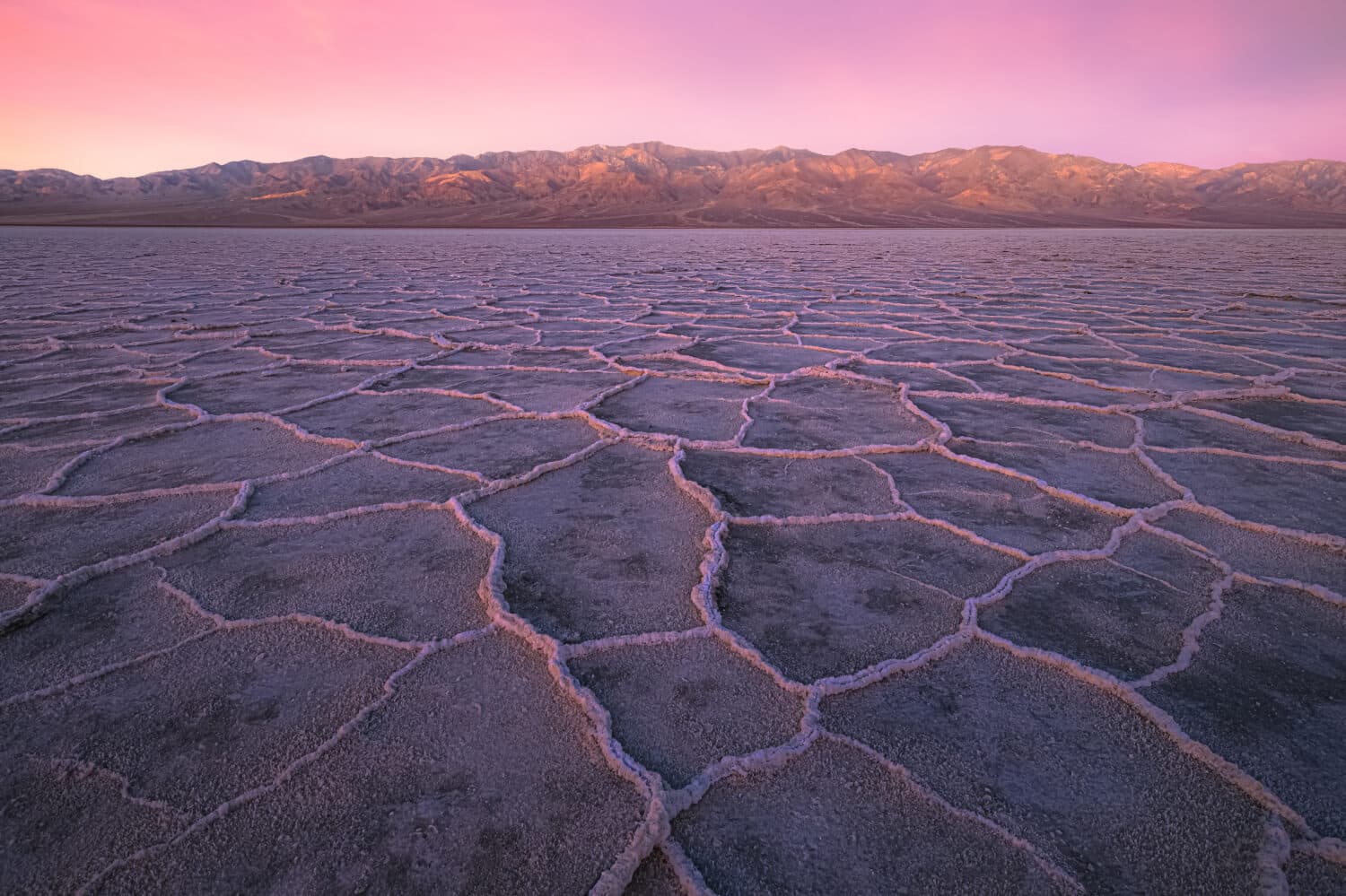 Beautiful, inspiring landscape and halite texture of Badwater Basin salt flats under a colourful, vibrant sunset or sunrise pink sky at Death Valley National Park, USA.