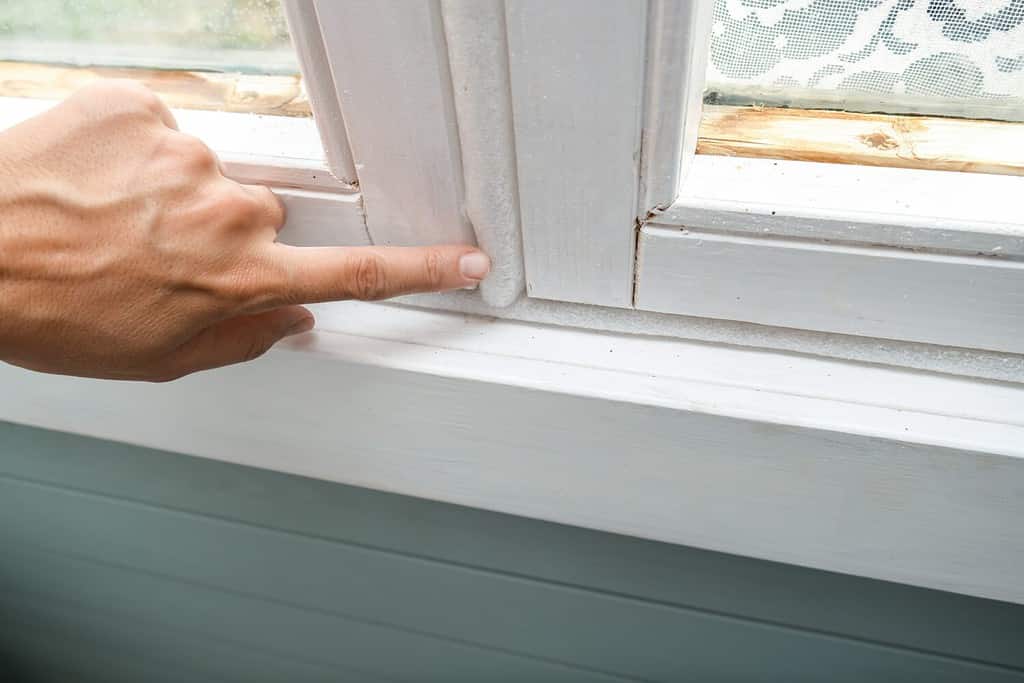 Woman hand insulating old windows to prevent warmth heat leak and drafts, preparing house for winter and cold weather