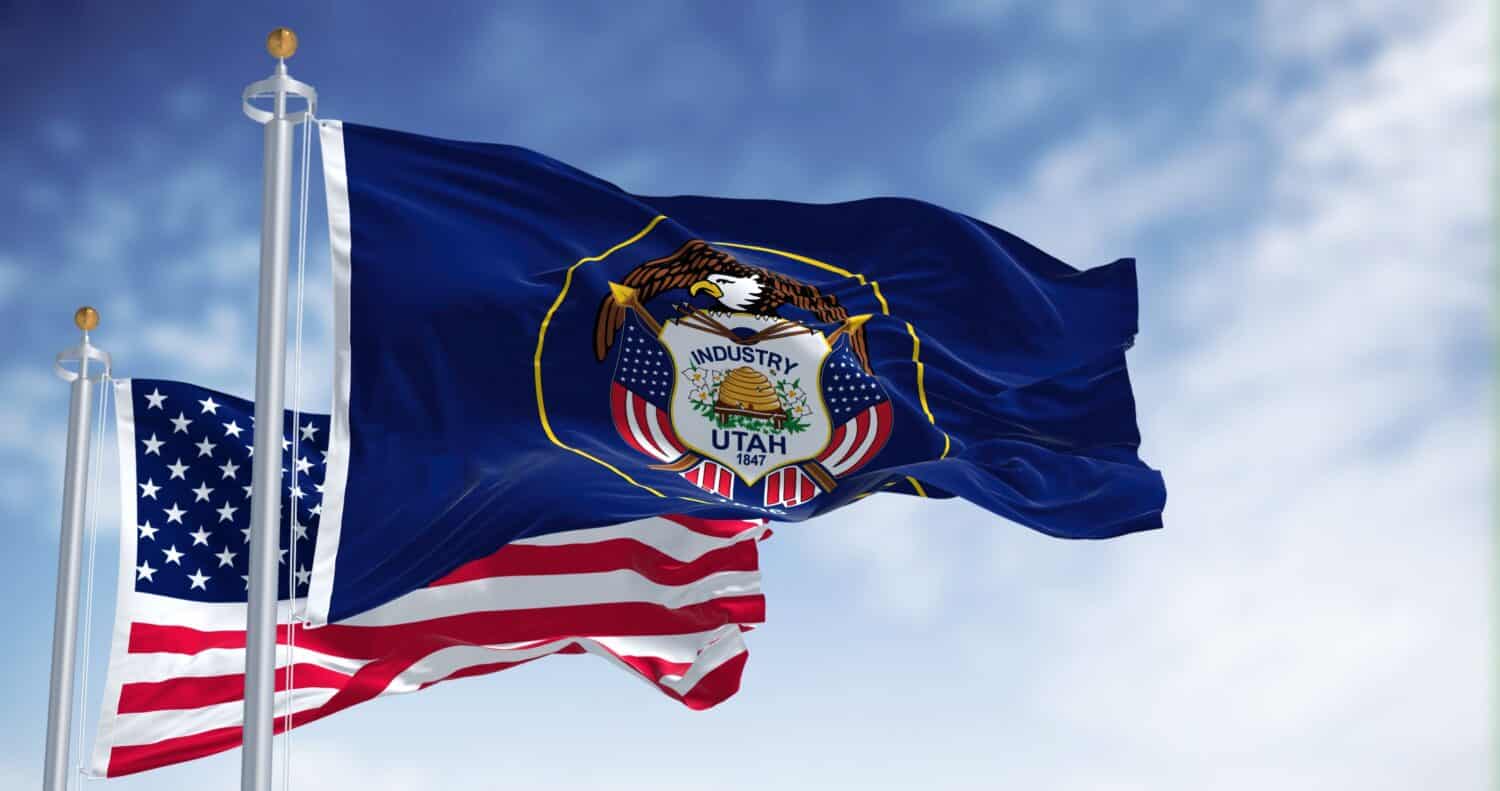 The Utah state flag waving along with the national flag of the United States of America. Utah is a state in the Mountain West subregion of the Western United States