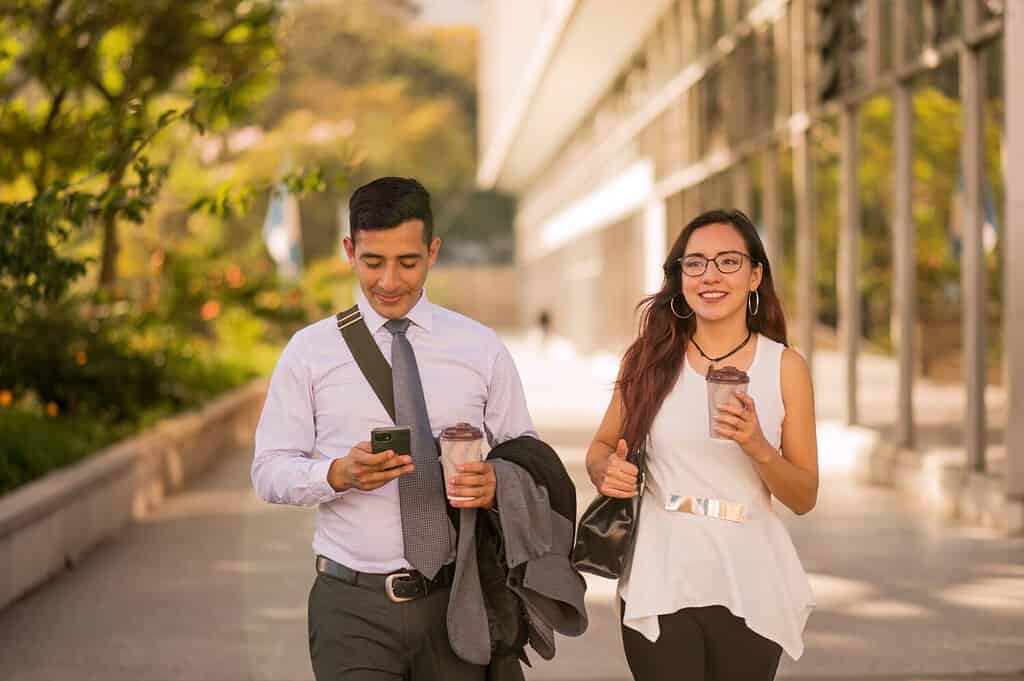 Latino man and woman walk through the financial center of Guatemala. Young business couple. Office workers walk in the city holding a cup of coffee.
