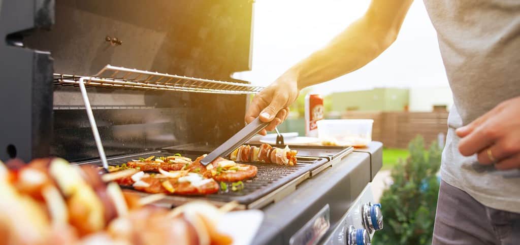 Young man grilling some kind of meats on the gas grill during lovely summer time, food concept