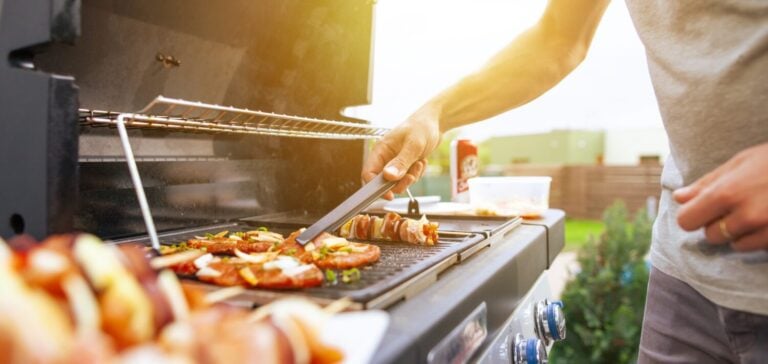 Young man grilling some kind of meats on the gas grill during lovely summer time, food concept
