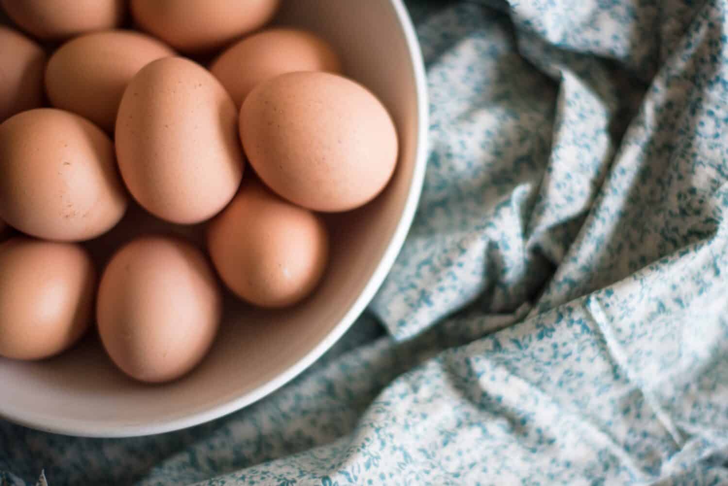 close up of brown eggs in a white bowl on floral fabric