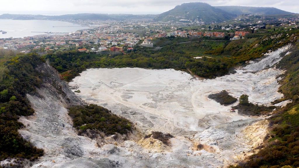 Aerial view of Solfatara of Pozzuoli, near Naples, Italy. It is a dormant volcano and part of the Phlegraean Fields volcanic area. In background there are Pozzuoli town and Mediterranean sea.