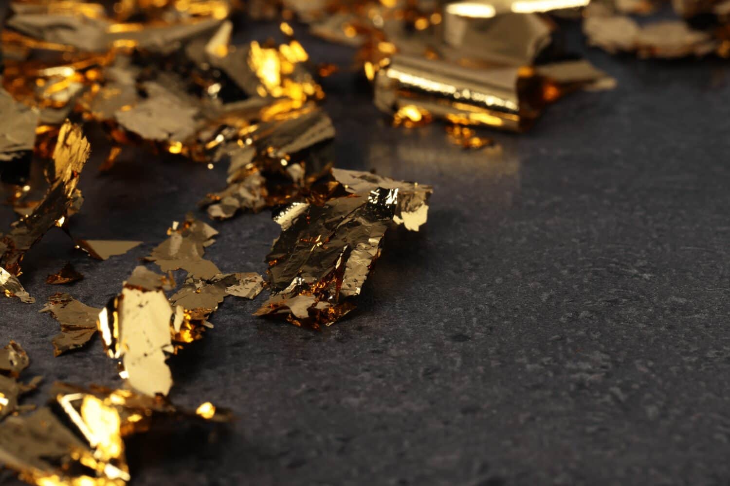 Pieces of edible gold leaf on textured table, closeup. Space for text
