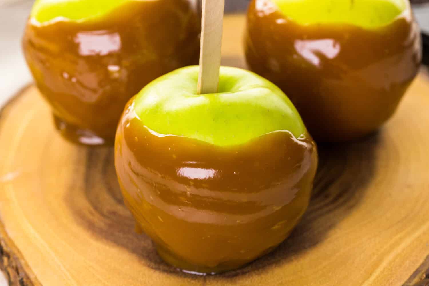 Apples freshly dipped in caramel on cutting board.